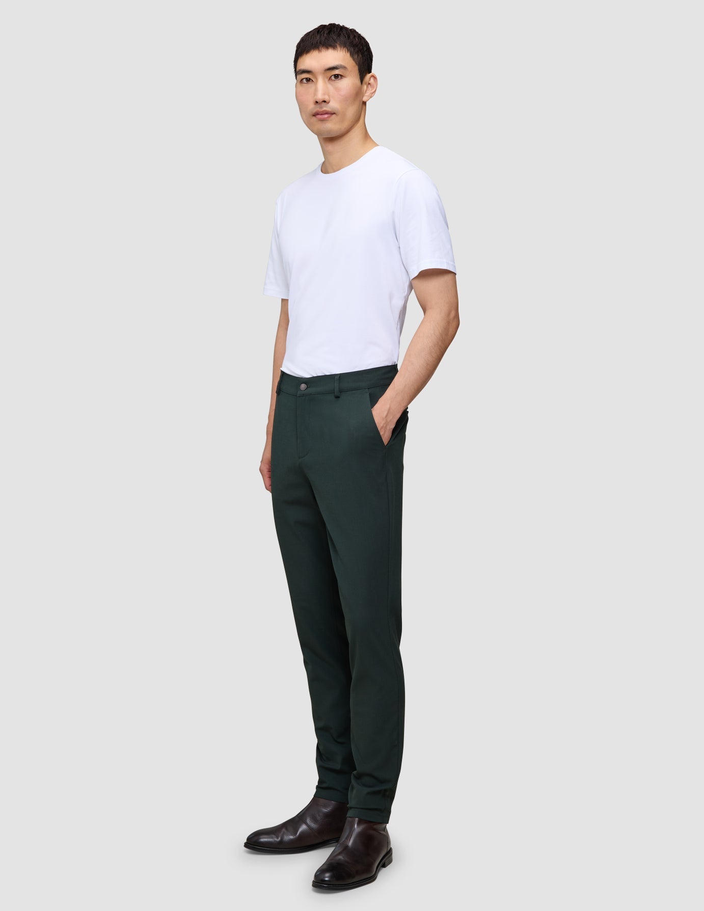 En man bär en vit t-shirt, Ease Pants Slim Northern Pine och mörka läderskor.